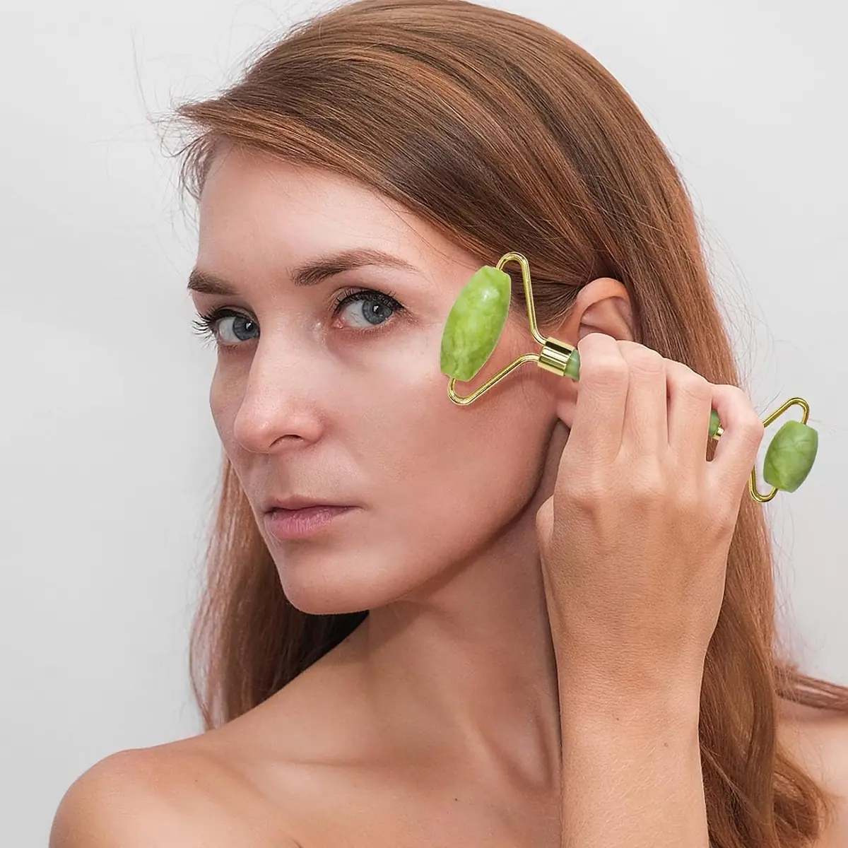 Person gently using a green facial roller along the cheek